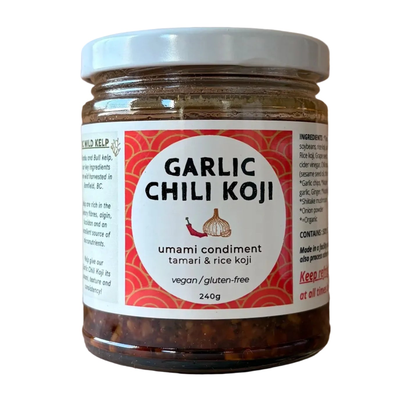 A jar of Garlic Chili Koji umami condiment on a light wood background. The clear glass jar shows the dark red chili paste inside, topped with a white lid and a white label with red and black text.