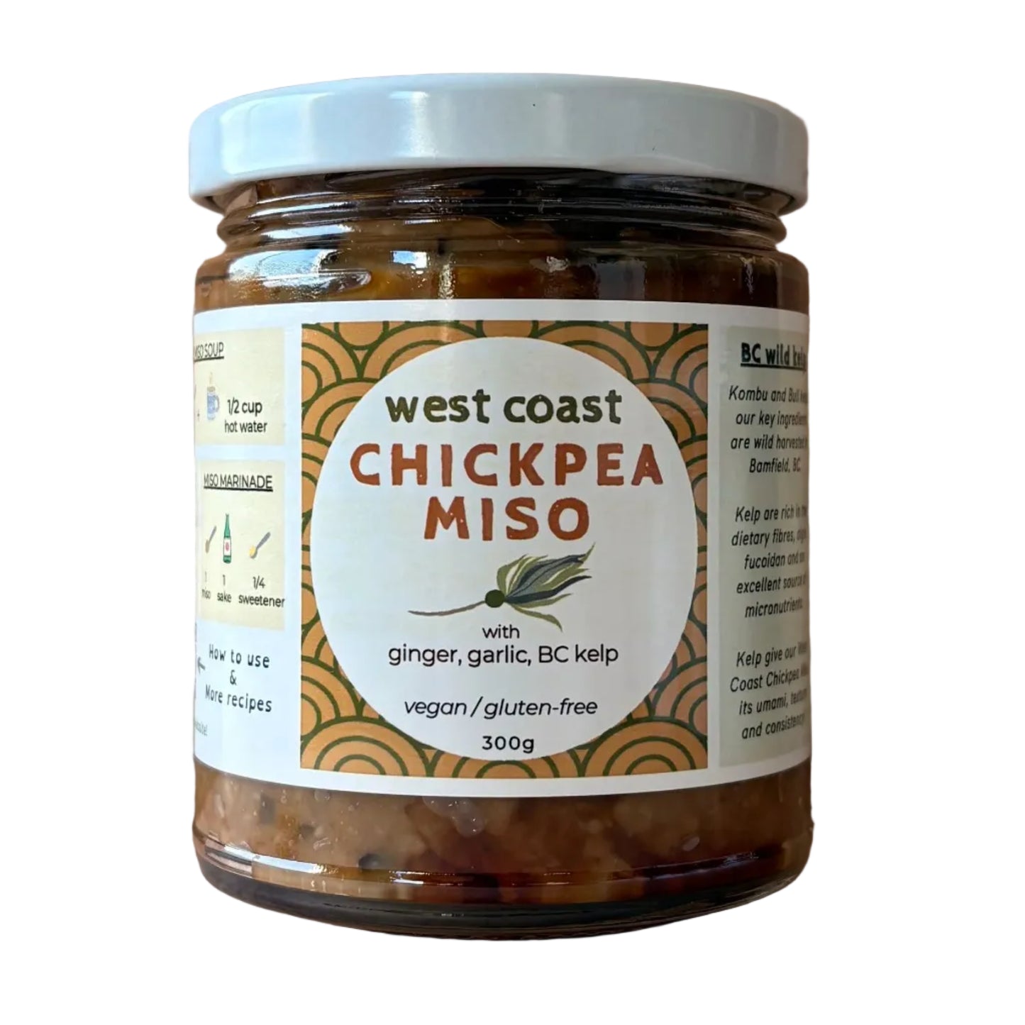 A jar of West Coast Chickpea Miso with a white lid and a cream-colored label, set on a light wood surface against a wooden plank background.