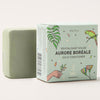 Green bar of soap next to its packaging on a white background