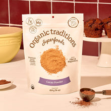 Bag of Organic Traditions Cacao Powder on a kitchen counter with baking items and a red tiled wall.