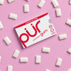 Box of PUR cinnamon gum on a pink background with gum pieces around
