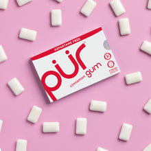 Box of PUR cinnamon gum on a pink background with gum pieces around